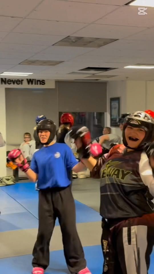 Two young Giroux Bros students in sparring gloves and head gear, smiling between rounds